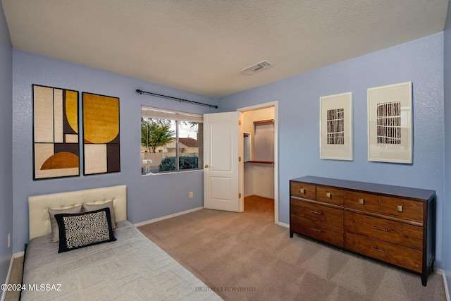 bedroom featuring light carpet, a textured ceiling, and a walk in closet