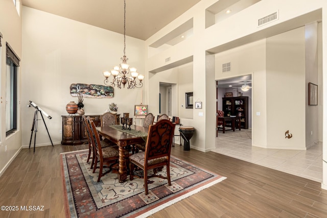 dining area featuring wood-type flooring, ceiling fan with notable chandelier, and a high ceiling