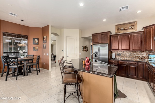 kitchen with light tile patterned flooring, a breakfast bar area, hanging light fixtures, a kitchen island with sink, and stainless steel fridge with ice dispenser