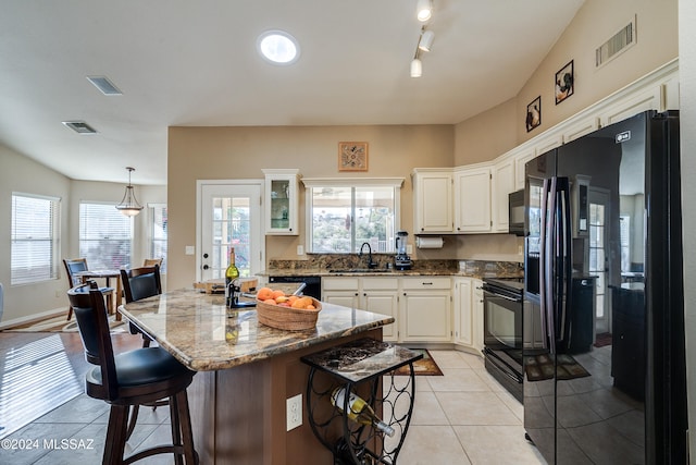 kitchen with light tile patterned floors, a center island, a wealth of natural light, and black appliances