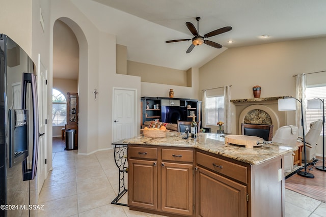 kitchen featuring light stone countertops, stainless steel fridge, a wealth of natural light, and an island with sink