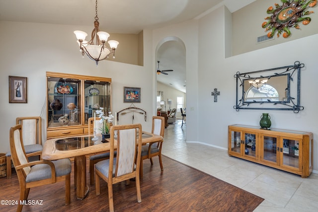 tiled dining area featuring ceiling fan with notable chandelier and high vaulted ceiling