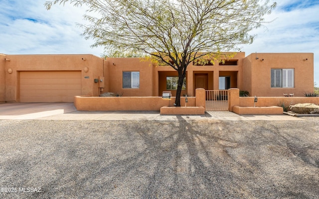 pueblo revival-style home with a garage, a fenced front yard, concrete driveway, and stucco siding