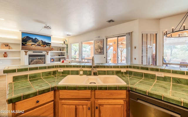 kitchen with visible vents, open floor plan, a sink, and a glass covered fireplace