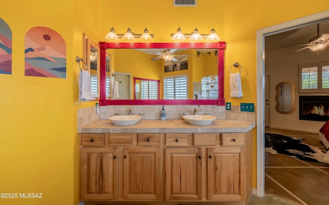 bathroom with visible vents, a lit fireplace, a sink, and a ceiling fan