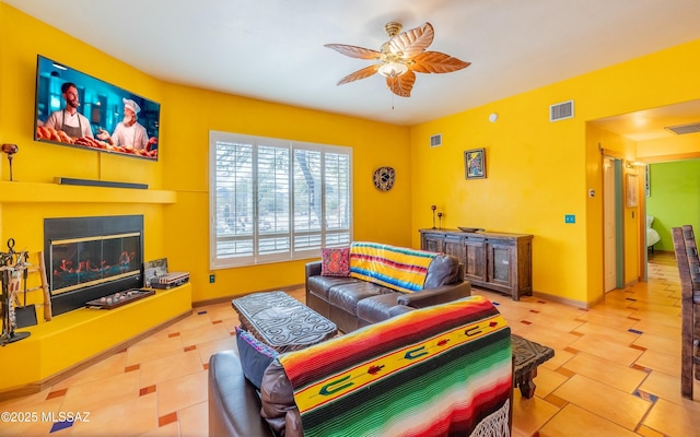 tiled living area with a ceiling fan, a glass covered fireplace, visible vents, and baseboards