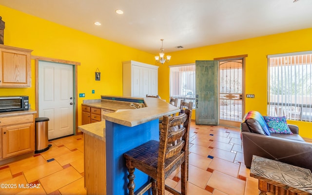 kitchen with a toaster, light countertops, light brown cabinetry, a kitchen bar, and a notable chandelier