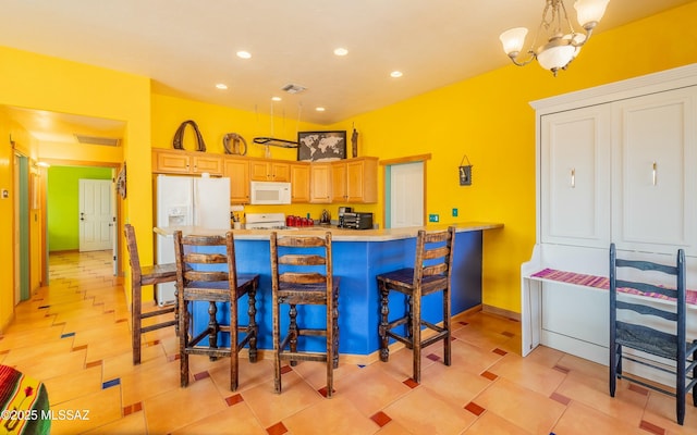 kitchen with a chandelier, a peninsula, white appliances, visible vents, and a kitchen breakfast bar