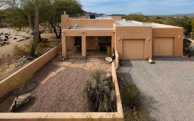 adobe home with driveway, a chimney, an attached garage, fence, and stucco siding