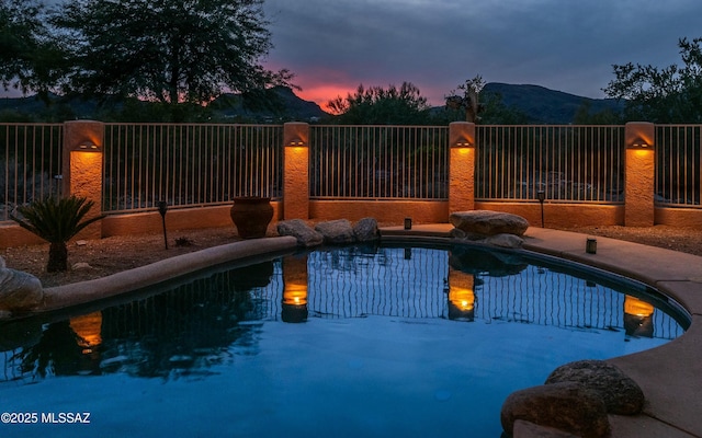 pool at dusk with an outdoor pool, fence, and a mountain view