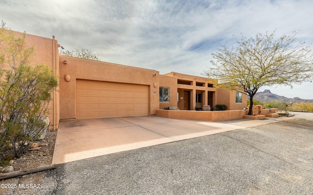 pueblo-style home with driveway, a garage, a mountain view, and stucco siding