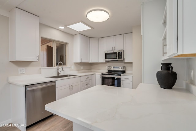 kitchen featuring sink, kitchen peninsula, stainless steel appliances, light stone countertops, and white cabinets