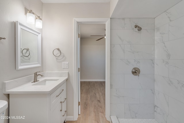 bathroom featuring toilet, a tile shower, vanity, hardwood / wood-style flooring, and ceiling fan