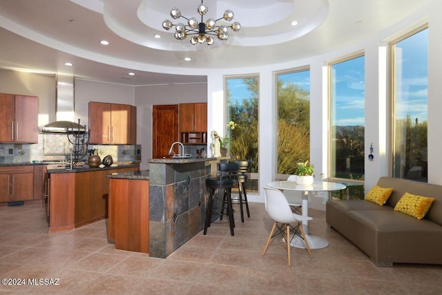 kitchen featuring a tray ceiling, backsplash, an island with sink, and ventilation hood