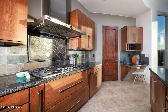 kitchen with dark stone counters, wall chimney exhaust hood, light tile patterned floors, tasteful backsplash, and stainless steel gas cooktop