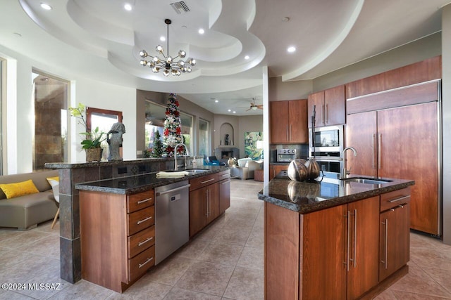 kitchen with a tray ceiling, stainless steel appliances, open floor plan, and an island with sink