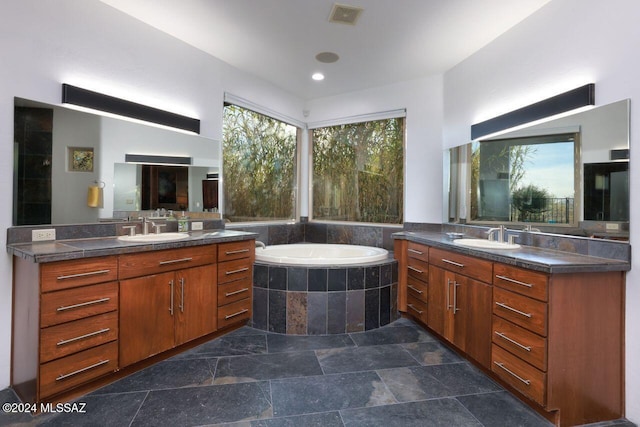 bathroom featuring a wealth of natural light, vanity, and a relaxing tiled tub