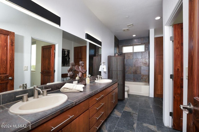 bathroom featuring toilet, double vanity, stone finish flooring, and a sink