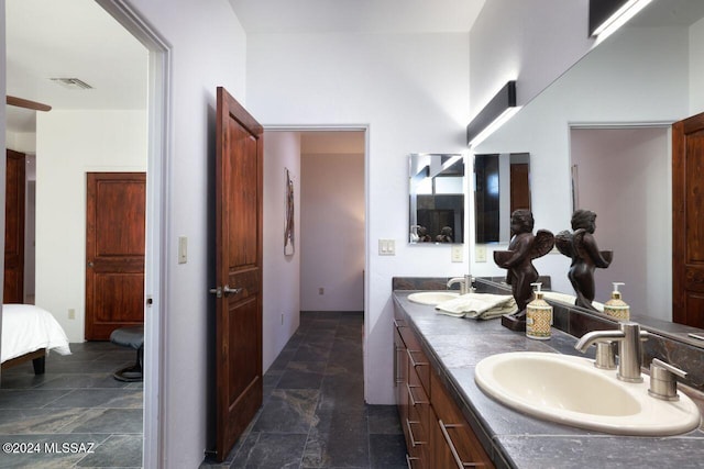 ensuite bathroom with a sink, visible vents, double vanity, and stone finish floor