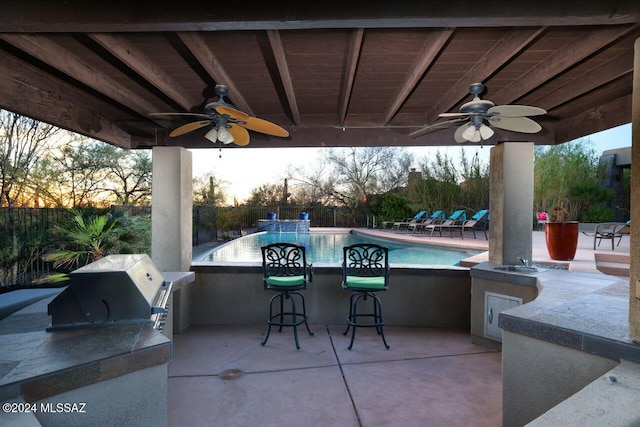 patio terrace at dusk with ceiling fan and an outdoor kitchen