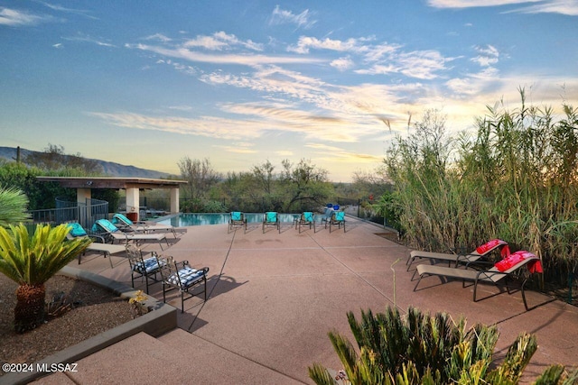 pool at dusk featuring a community pool, a patio area, and fence