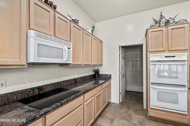 kitchen featuring light brown cabinets, white appliances, and dark stone counters