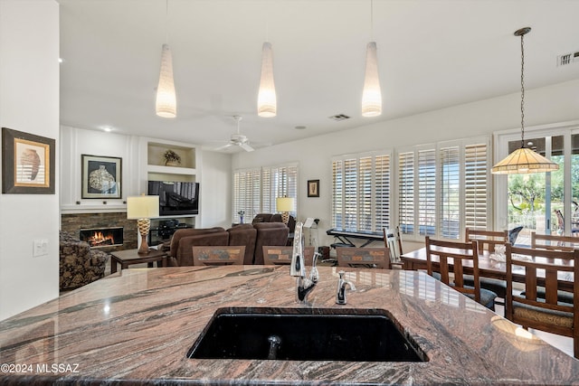 kitchen featuring sink, ceiling fan, built in features, a fireplace, and stone countertops