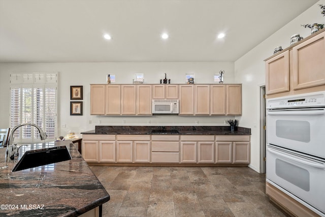 kitchen featuring dark stone countertops, sink, white appliances, and light brown cabinets