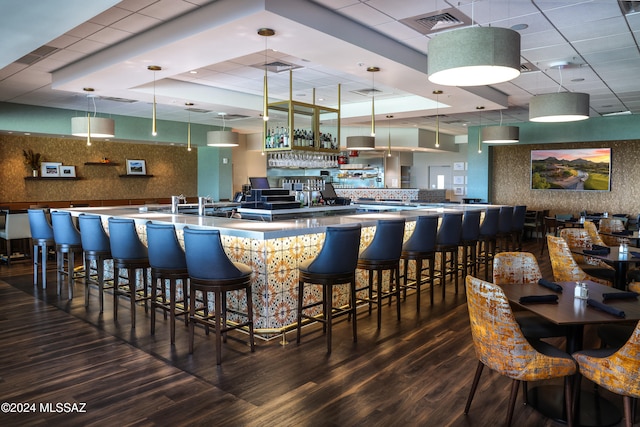 bar featuring a raised ceiling, dark hardwood / wood-style flooring, a drop ceiling, and hanging light fixtures