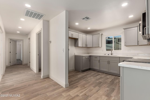 kitchen featuring visible vents, light wood finished floors, gray cabinets, and a sink