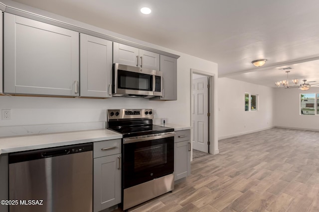 kitchen with stainless steel appliances, light wood-type flooring, a chandelier, gray cabinetry, and light countertops