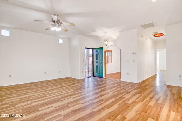 unfurnished room with ceiling fan with notable chandelier, light hardwood / wood-style floors, and a wealth of natural light