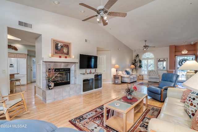 living room featuring ceiling fan, light hardwood / wood-style floors, high vaulted ceiling, and a tiled fireplace