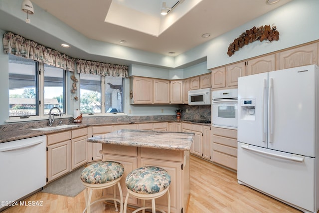 kitchen featuring sink, a center island, white appliances, a kitchen bar, and light wood-type flooring