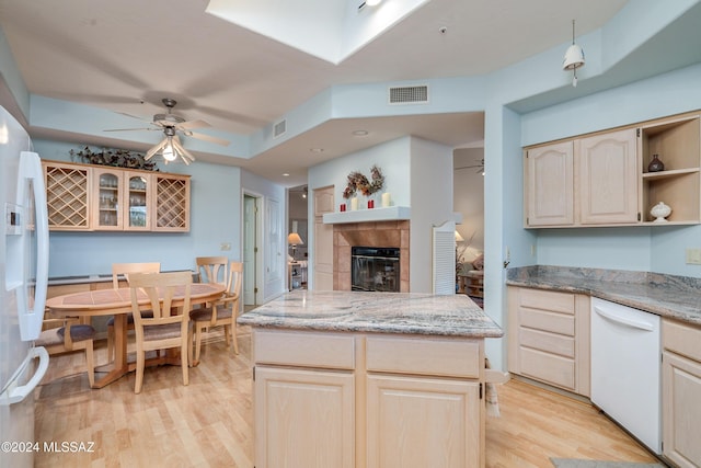 kitchen featuring light brown cabinets, white appliances, light hardwood / wood-style floors, and a tiled fireplace