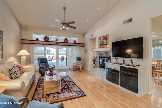 living room featuring ceiling fan, french doors, high vaulted ceiling, light hardwood / wood-style floors, and a fireplace