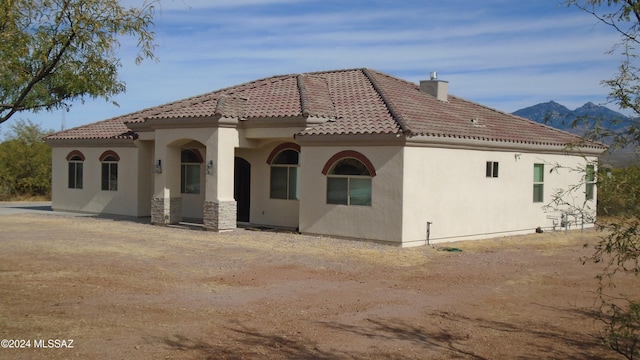 back of house with a tile roof, a chimney, and stucco siding