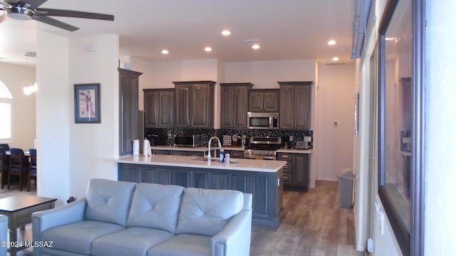 kitchen featuring open floor plan, stainless steel appliances, dark brown cabinets, light countertops, and backsplash