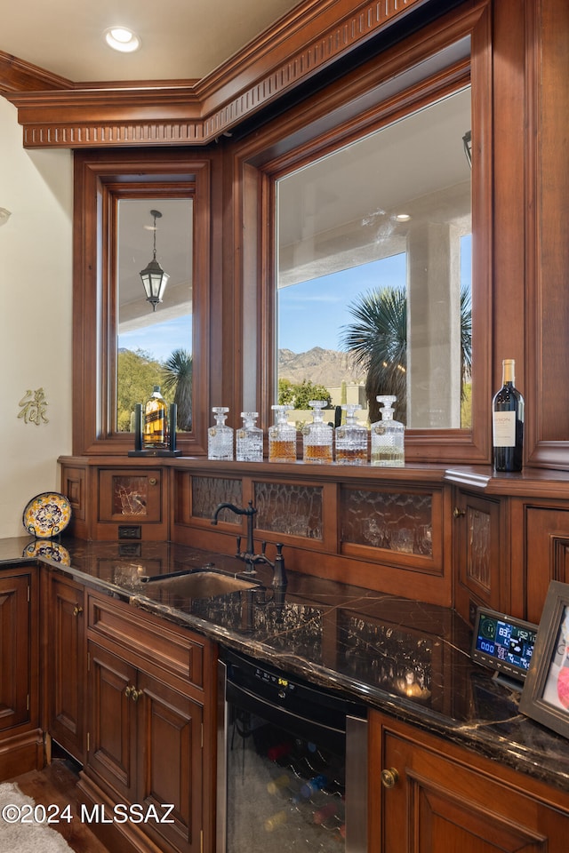 bar featuring dark stone counters, beverage cooler, crown molding, sink, and a mountain view