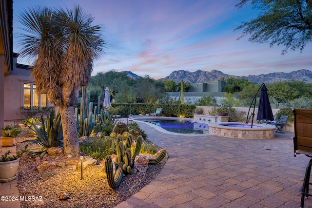 pool at dusk with pool water feature, a mountain view, an in ground hot tub, and a patio