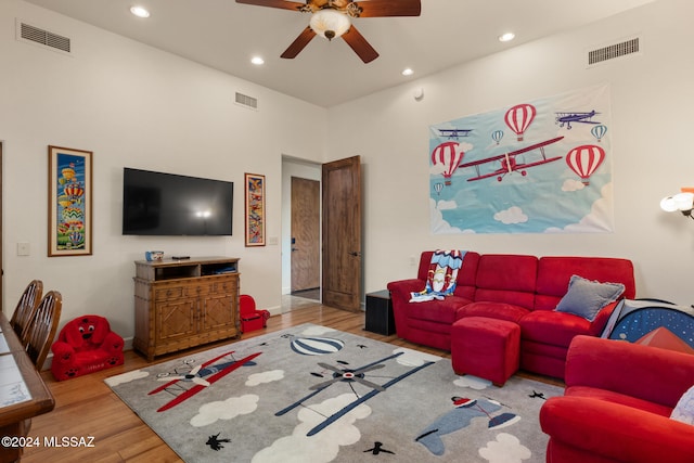 living room featuring ceiling fan, a high ceiling, and light wood-type flooring