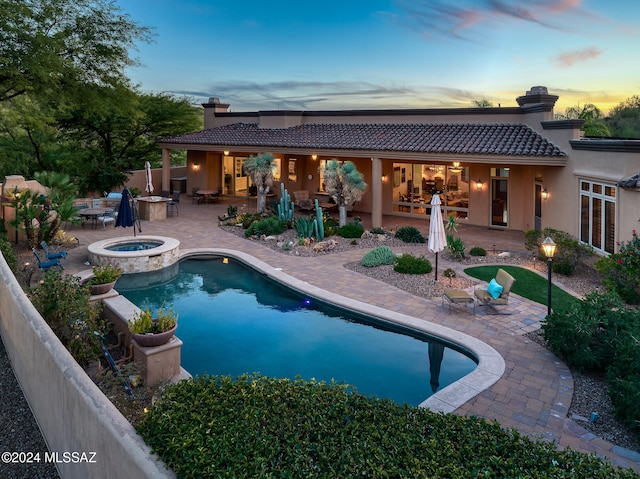 pool at dusk featuring a patio area and an in ground hot tub