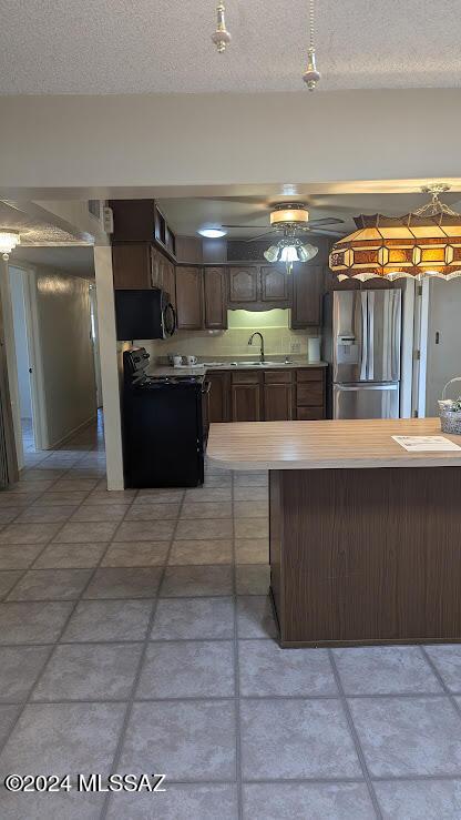 kitchen with a breakfast bar, a textured ceiling, dark brown cabinetry, sink, and black appliances