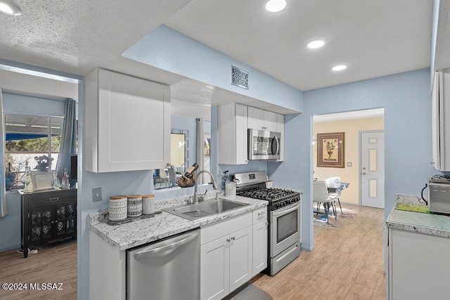 kitchen featuring white cabinets, sink, light wood-type flooring, a textured ceiling, and stainless steel appliances