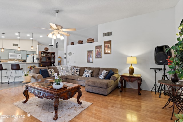 living room with ceiling fan, light wood-type flooring, a textured ceiling, and high vaulted ceiling