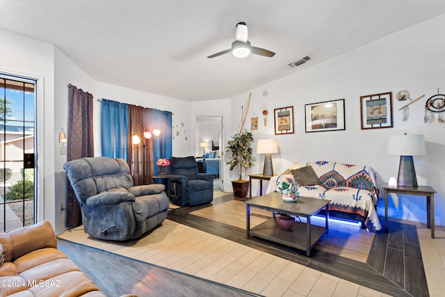 living room featuring ceiling fan, light wood-type flooring, and a textured ceiling