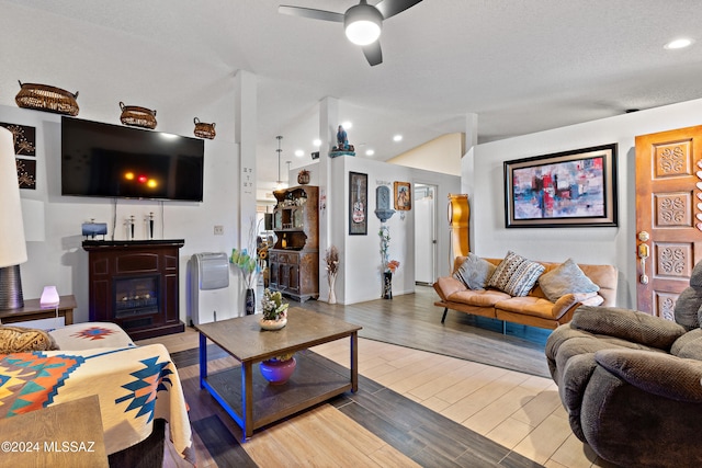 living room with ceiling fan, light hardwood / wood-style floors, a textured ceiling, and vaulted ceiling