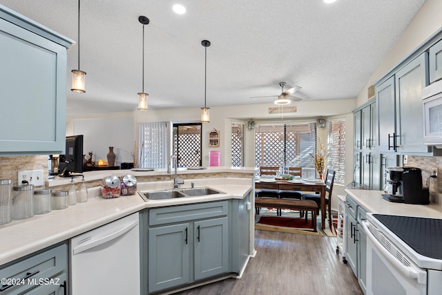 kitchen with backsplash, white appliances, sink, pendant lighting, and hardwood / wood-style flooring