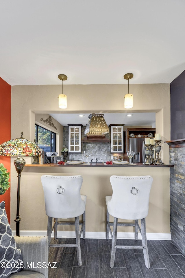 kitchen with hanging light fixtures, stainless steel fridge with ice dispenser, premium range hood, kitchen peninsula, and decorative backsplash