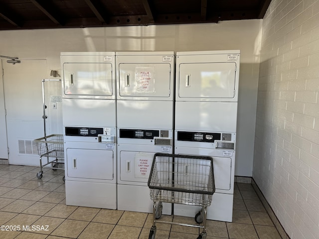 laundry area featuring light tile patterned floors, brick wall, and stacked washer / drying machine